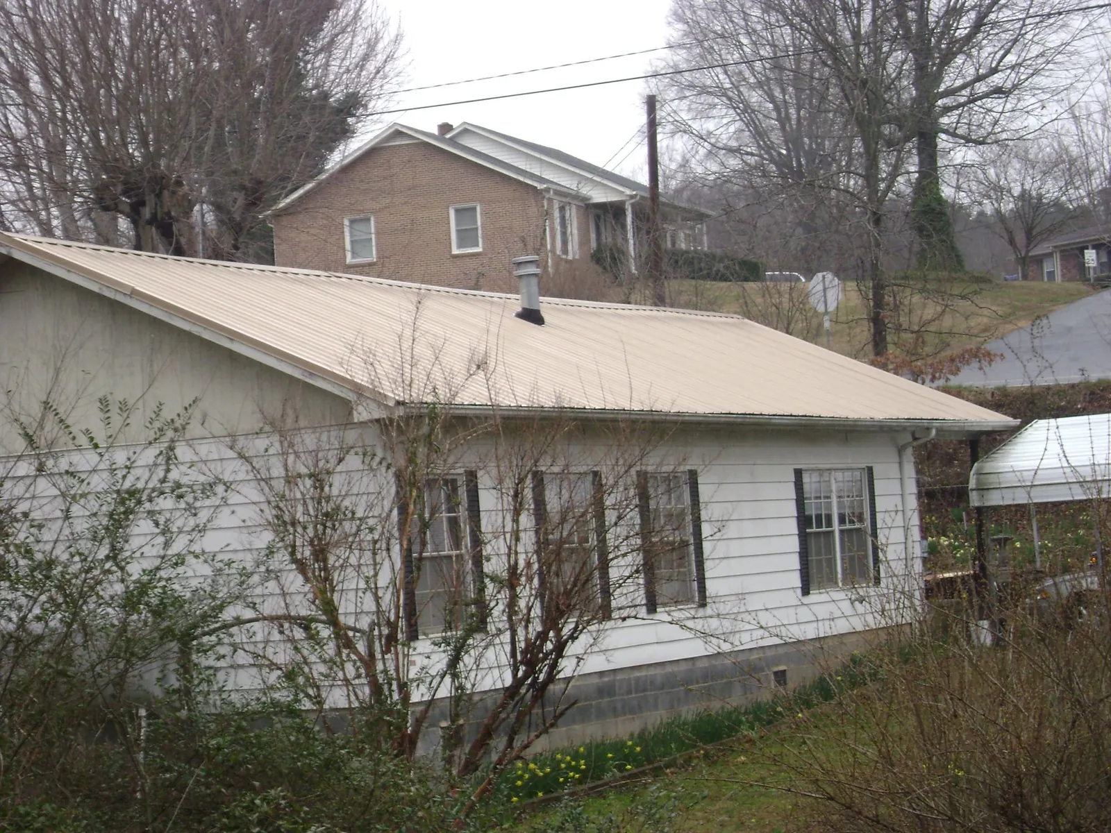 Tan metal roof on a white sided house set into a hillside — Commercial Roofing by Roofing Brothers in Apopka
